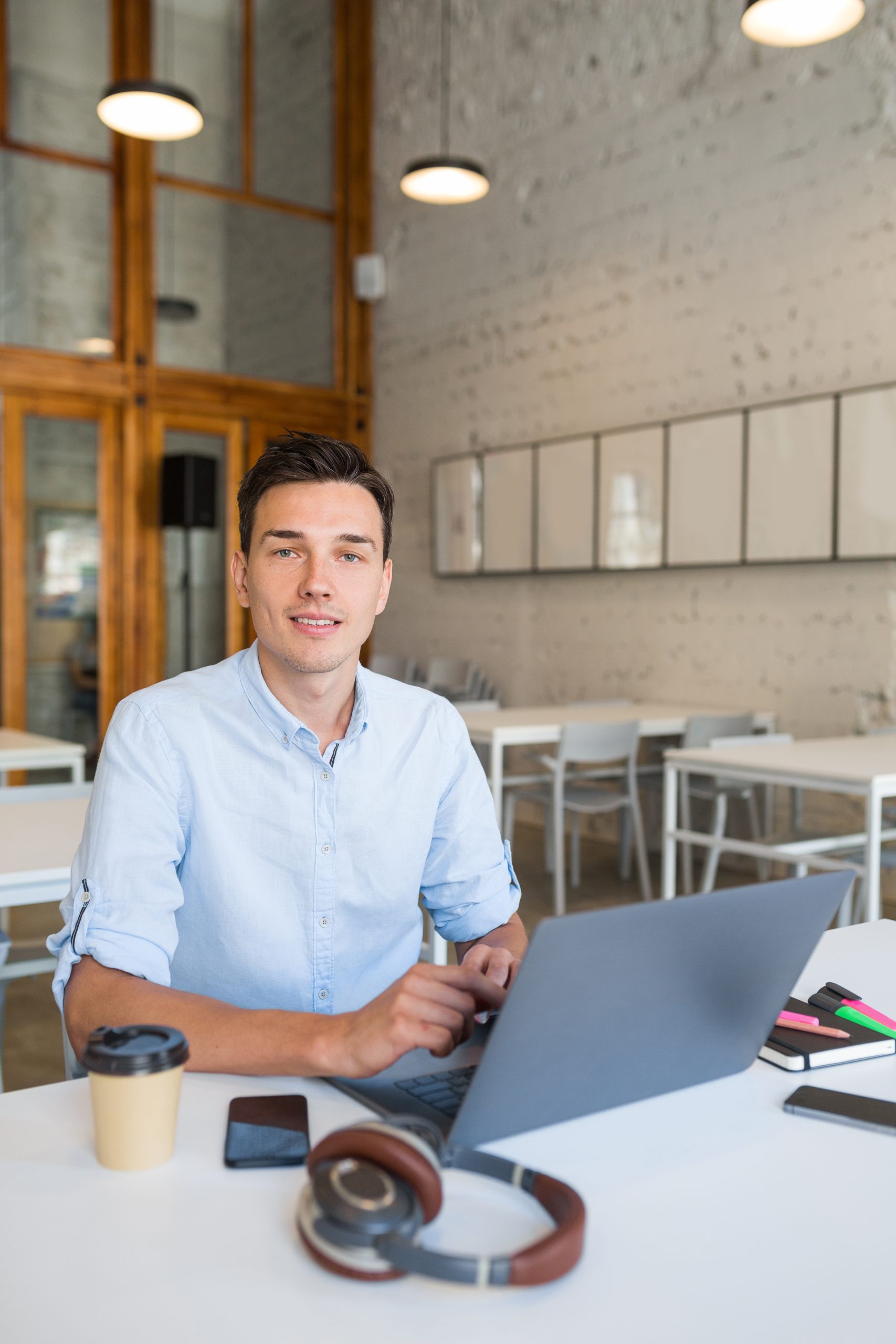young handsome smiling man sitting in open space office working on laptop, happy, positive, successful modern youth, online education